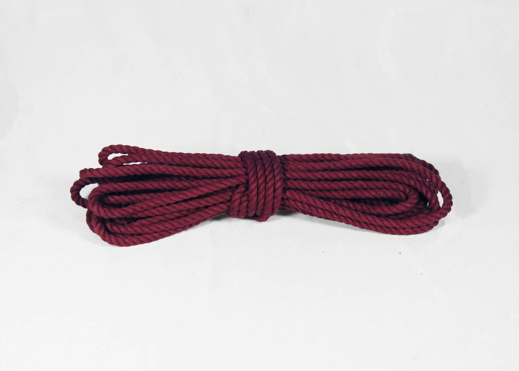 A coiled bundle of braided cotton rope in a deep burgundy or maroon colour, photographed on a plain white background.