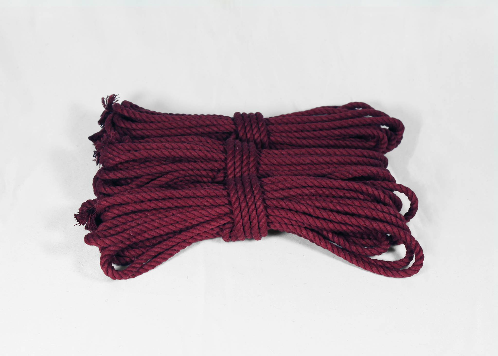A coiled bundle of dark burgundy twisted rope, photographed against a plain white background.