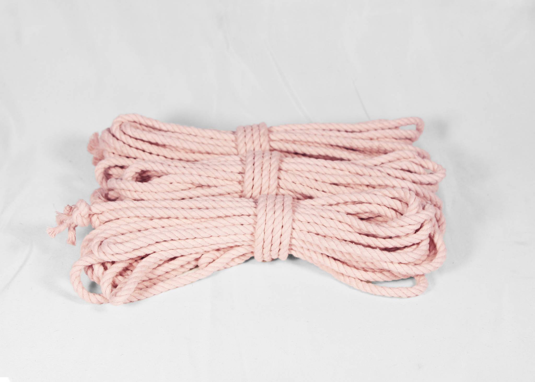 A coiled bundle of light pink cotton rope or cord, tied in the center, displayed on a white fabric background.